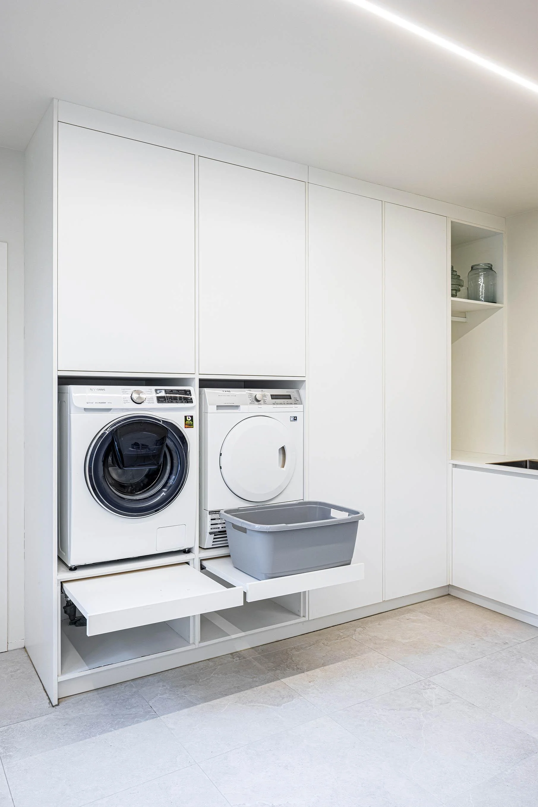 Opbergruimte rondom wasmachine en droogkast en uittrekbare lades voor wasmand